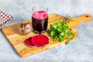 Bir bardak pancar suyu, taze pancar dilimleri, bir pancar kökü ve tahta üzerinde nane yaprakları..