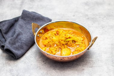 Hint usulü bakır bir tabakta servis edilen karnabahar ve patatesli bir kase canlı sarı köri..