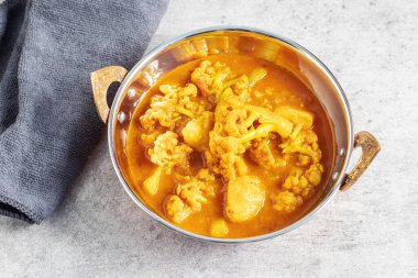 Hint usulü bakır bir tabakta servis edilen karnabahar ve patatesli bir kase canlı sarı köri..