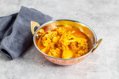 Hint usulü bakır bir tabakta servis edilen karnabahar ve patatesli bir kase canlı sarı köri..