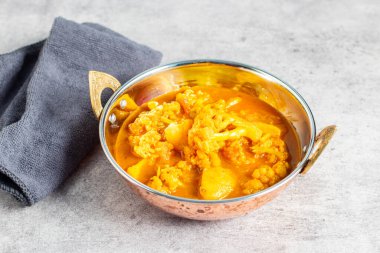 Hint usulü bakır bir tabakta servis edilen karnabahar ve patatesli bir kase canlı sarı köri..