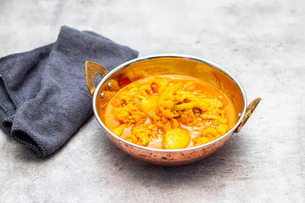 Hint usulü bakır bir tabakta servis edilen karnabahar ve patatesli bir kase canlı sarı köri..