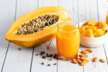 A halved papaya, vibrant smoothie in a glass jar with a straw, fresh cubes in a bowl, and scattered seeds on a wooden board clipart