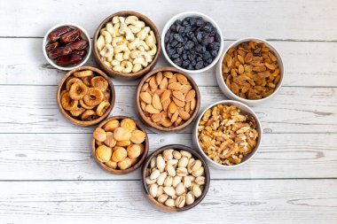 Kurumuş meyve ve fındık çeşitleri beyaz ahşap bir yüzeye yerleştirilmiş, hurma, kaju, badem, kuru üzüm, incir, kayısı ve ceviz de dahil olmak üzere..