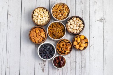 Kurumuş meyve ve fındık çeşitleri beyaz ahşap bir yüzeye yerleştirilmiş, hurma, kaju, badem, kuru üzüm, incir, kayısı ve ceviz de dahil olmak üzere..