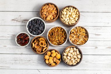 Kurumuş meyve ve fındık çeşitleri beyaz ahşap bir yüzeye yerleştirilmiş, hurma, kaju, badem, kuru üzüm, incir, kayısı ve ceviz de dahil olmak üzere..