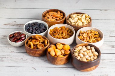 Kurumuş meyve ve fındık çeşitleri beyaz ahşap bir yüzeye yerleştirilmiş, hurma, kaju, badem, kuru üzüm, incir, kayısı ve ceviz de dahil olmak üzere..