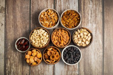 Kurumuş meyve ve fındık çeşitleri beyaz ahşap bir yüzeye yerleştirilmiş, hurma, kaju, badem, kuru üzüm, incir, kayısı ve ceviz de dahil olmak üzere..