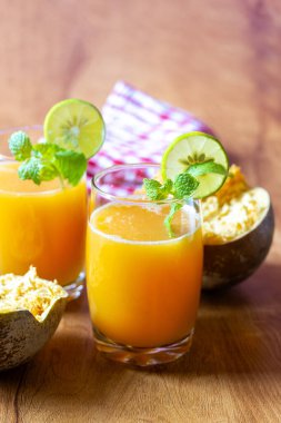 İki bardak bael suyu, limon ve nane ile süslenmiş ahşap bir masada. Taze limonlarla çevrili ve arka planda bael meyvesi var..