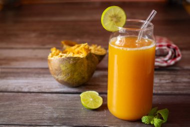 Limon ve nane ile süslenmiş ferahlatıcı bir bardak Bael meyve suyu, yanında da köy ahşabı bir masada yarım yamalak bael meyvesi ve limon dilimleri..