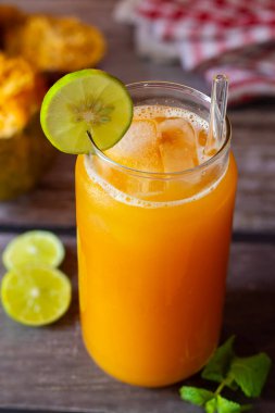 Limon ve nane ile süslenmiş ferahlatıcı bir bardak Bael meyve suyu, yanında da köy ahşabı bir masada yarım yamalak bael meyvesi ve limon dilimleri..