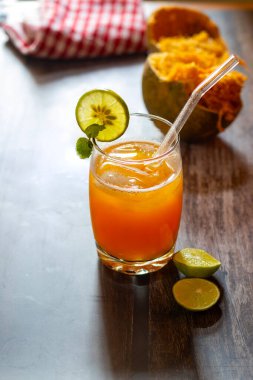 Limon ve nane ile süslenmiş ferahlatıcı bir bardak Bael meyve suyu, yanında da köy ahşabı bir masada yarım yamalak bael meyvesi ve limon dilimleri..