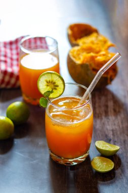 İki bardak bael suyu, limon ve nane ile süslenmiş ahşap bir masada. Taze limonlarla çevrili ve arka planda bael meyvesi var..
