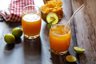 İki bardak bael suyu, limon ve nane ile süslenmiş ahşap bir masada. Taze limonlarla çevrili ve arka planda bael meyvesi var..