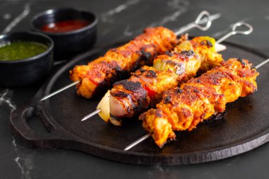 Yanında doğranmış domates, soğan, misket limonu ve sosla servis edilen demir bir tavada sebzeli ızgara tavuk şişleri..