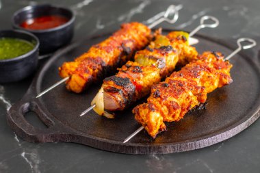 Yanında doğranmış domates, soğan, misket limonu ve sosla servis edilen demir bir tavada sebzeli ızgara tavuk şişleri..