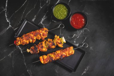 Yanında doğranmış domates, soğan, misket limonu ve sosla servis edilen demir bir tavada sebzeli ızgara tavuk şişleri..