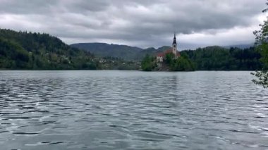 Slovenya 'daki Bled Gölü' nün ortasında güzel dağlar ve küçük bir ada. Bulutlu yağmurlu hava, su yansıması nazik hareket. Yüksek kalite 4k görüntü