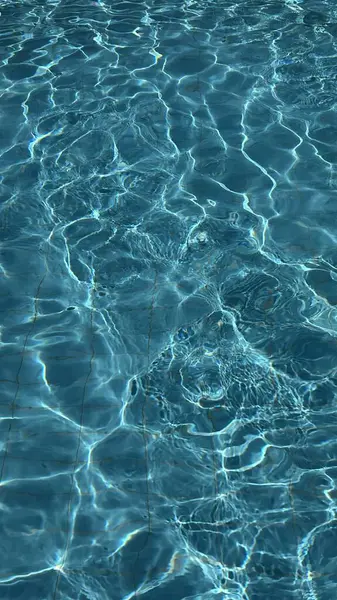 Yüzme havuzunda güneş yansıması olan derin mavi dalgalı suyun dikey fotoğrafı. Yüksek kalite fotoğraf