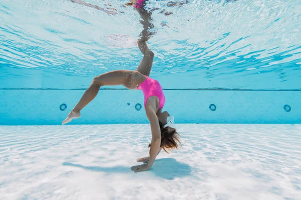 身穿粉色比基尼的年轻女子在游泳池里表演水下杂技 — 图库照片