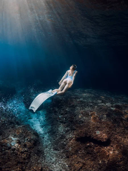 女性のフリーダイバーは水中で白いフィンで滑ります フリーダイビングとともに美しいです女の子で深海と素晴らしい太陽光線 — ストック写真