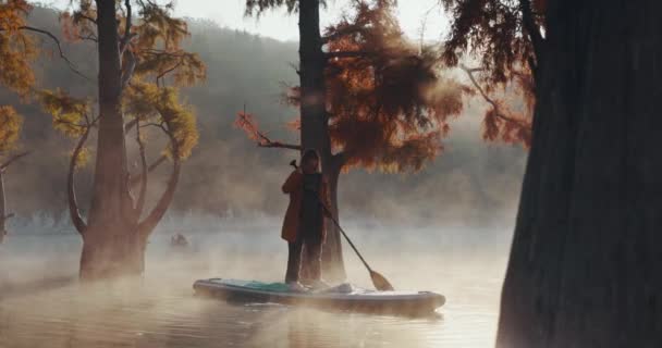 2021年10月28日 ロシアのスカコ 霧と秋のタクソディウムの木と湖の上のパドルボード上の女性 — ストック動画