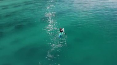 Man on stand up paddle board in blue sea. Surfer training on SUP board in summer sea. Aerial view