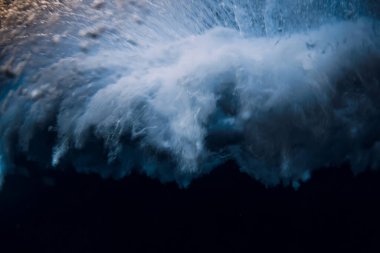 Wave with foam and air bubbles crash in ocean. Underwater view of ocean wave