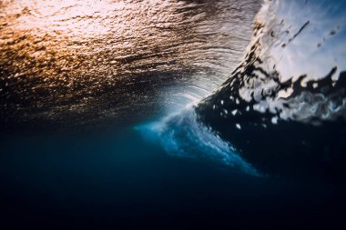 Barrel wave crash in ocean with sunset or sunrise light. Underwater view of surfing wave