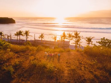 Aerial view with sunset light and tropical coastline with group of people. Ocean waves on Balangan beach in Bali.