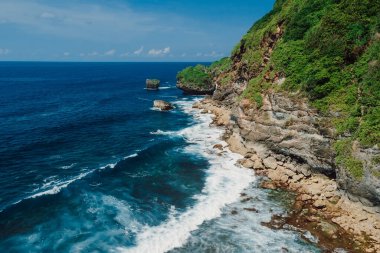 Scenic coastline with rocks and transparent ocean with waves in Bali. Aerial view.