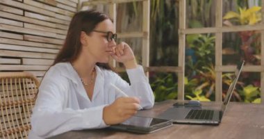 Woman work on touch pad with laptop while sitting near window in creative office or cafe