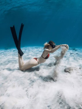 Free diver lady in bikini with sand in hands over sandy bottom. Freediving in tropical blue ocean with attractive woman