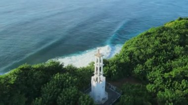 Aerial view of white lighthouse and scenic coastline, sunshine and ocean with waves in Bali