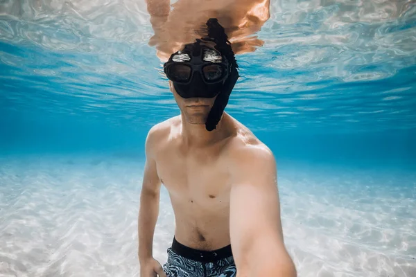 Man freediver in diving mask make selfie underwater over sandy bottom in blue ocean water. Activity vacation in tropical sea.