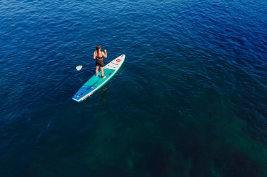 24 Temmuz 2022. Antalya, Türkiye. Mavi denizde ayağa kalkmış kürek çeken kadın. Okyanustaki Kırmızı Kürek SUP tahtasıyla antrenman. Hava görünümü