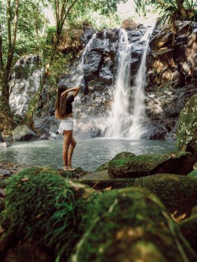 Tropikal Bali 'de şelalede güzel, zayıf bir kadın. Nehirde şelaleyle poz veren gezgin kız.