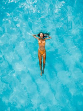 Güzel bir kadın şeffaf mavi okyanusta dinleniyor ve yüzüyor. Hava görünümü, üst görünüm.