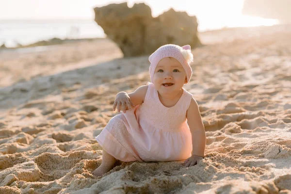 Dışarıda gün batımında gülümseyen güzel bir kız. Okyanus sahilinde pembe elbiseli mutlu bebek.