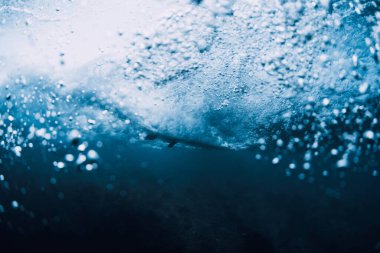 Suyun altında dalgalar ve sörfçüler okyanusta sörf tahtasıyla gezerler. Suyun altında dalgalar ve sörf tahtaları şeffaf suda çarpışır.