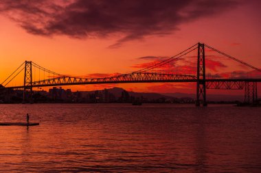 Günbatımı gökyüzü ve Brezilya 'nın Florianopolis kentindeki suda yansıyan eski kablo köprüsünün silüeti.