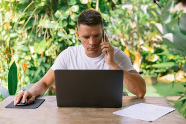Yazılım tasarımcısı telefonda müşterisiyle yeni bir projeyi tartışıyor. Açık bir planlama ofisinde dizüstü bilgisayarda çalışan ciddi bir adam..