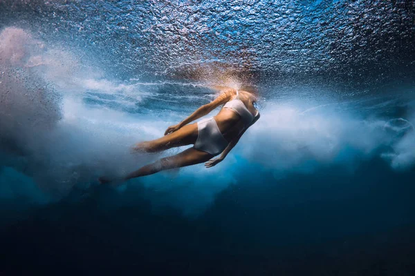 Woman dive under ocean wave. Duck dive under crashing barrel wave in transparent ocean