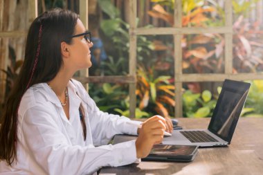 Dışarıdaki ofiste dijital tablet ve dizüstü bilgisayar kullanan genç kadın tasarımcı.