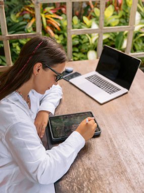 Dışarıdaki ofiste dijital tablet ve dizüstü bilgisayar kullanan genç kadın tasarımcı.