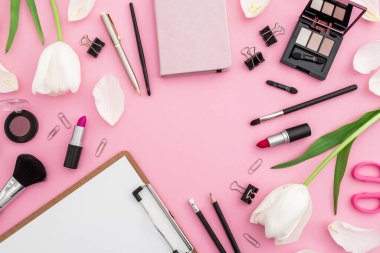 Pano, çiçekler, kozmetik ürünleri ve pembe arka planda izole edilmiş aksesuarlı güzel kadın blog yazarı kompozisyonu. Üst Manzara. Düz yatıyordu.