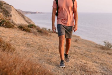 Sırt çantalı yürüyüşçünün alt tarafı sıcak güneş ışığıyla kıyıda yürüyor..