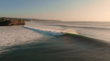 Büyük dalgalarda sörf yapan kıyı şeridinin havadan görüntüsü. Sıcak günbatımı tonlarında mükemmel okyanus dalgaları
