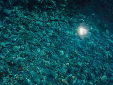 Güneşli bir günde mavi okyanus suyu, hava manzarası. Taştan deniz tabanına sahip şeffaf deniz arka planı. Üst görünüm 