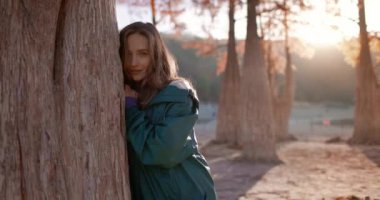 Çekici, mutlu kadın sonbahar parkında yürüyor ve kameraya bakıyor. Gün batımında doğada güzel bir kız. Aktif yaşam tarzı. Ormandaki insanlar.